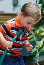 little boy drinking from a garden hose